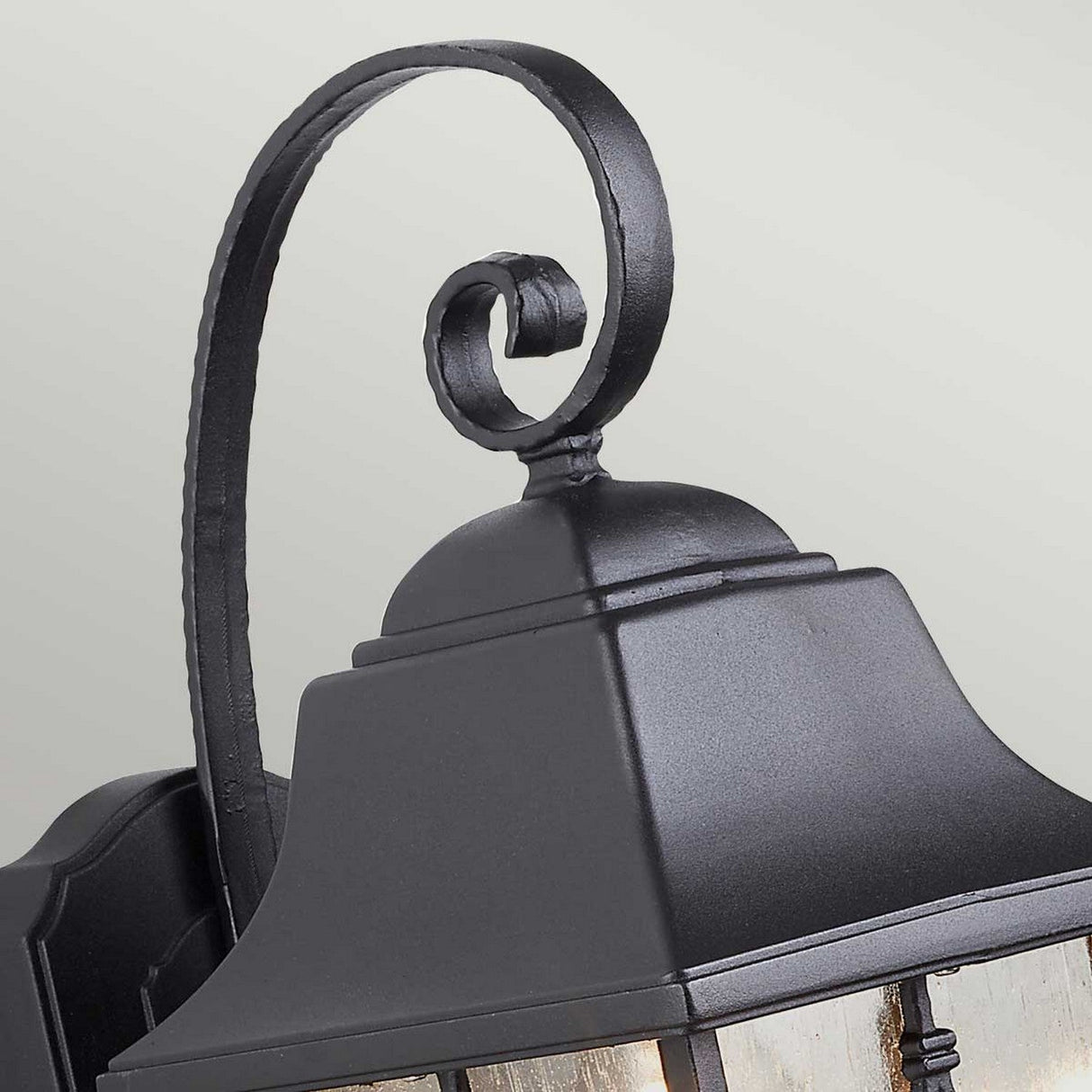 A close-up of the Kent 1 Light Outdoor Wall Light - Black highlights its elegant scroll design, rectangular shape, and peaked roof. This IP44 rated fixture with a black finish is ideal for mounting on an exterior wall.