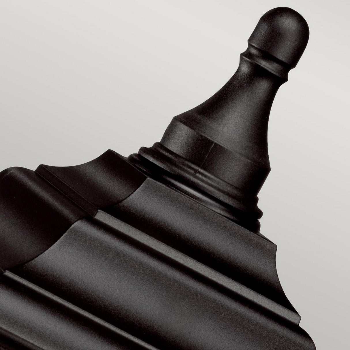 A close-up view of the Kerry 1 Light Pedestal/Porch in black showcases its corrosion-proof finial with a smooth, matte finish and rounded, tapered geometric shapes. Set against a neutral gray background, it exudes an elegant touch reminiscent of a porch light, emphasizing its ornate and symmetrical design.