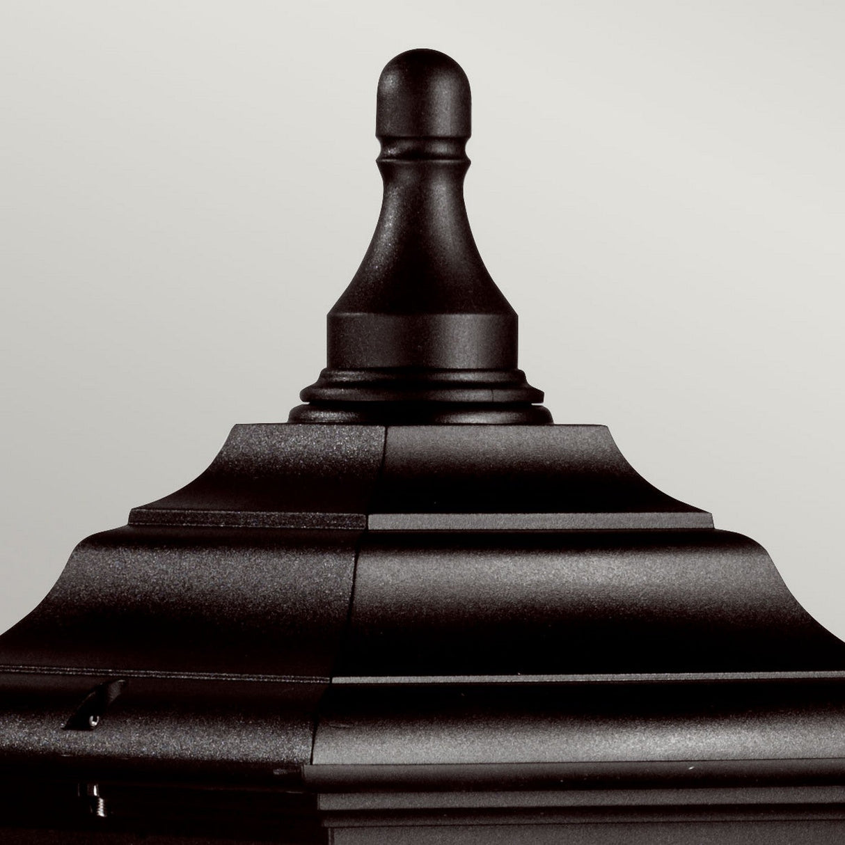 A close-up of the Kerry 1 Light Pillar Light in black, showcasing its metal finial with tiered layers culminating in a rounded top. This impact-resistant piece, perfect for outdoor lighting, stands out against the simple, light gray background.