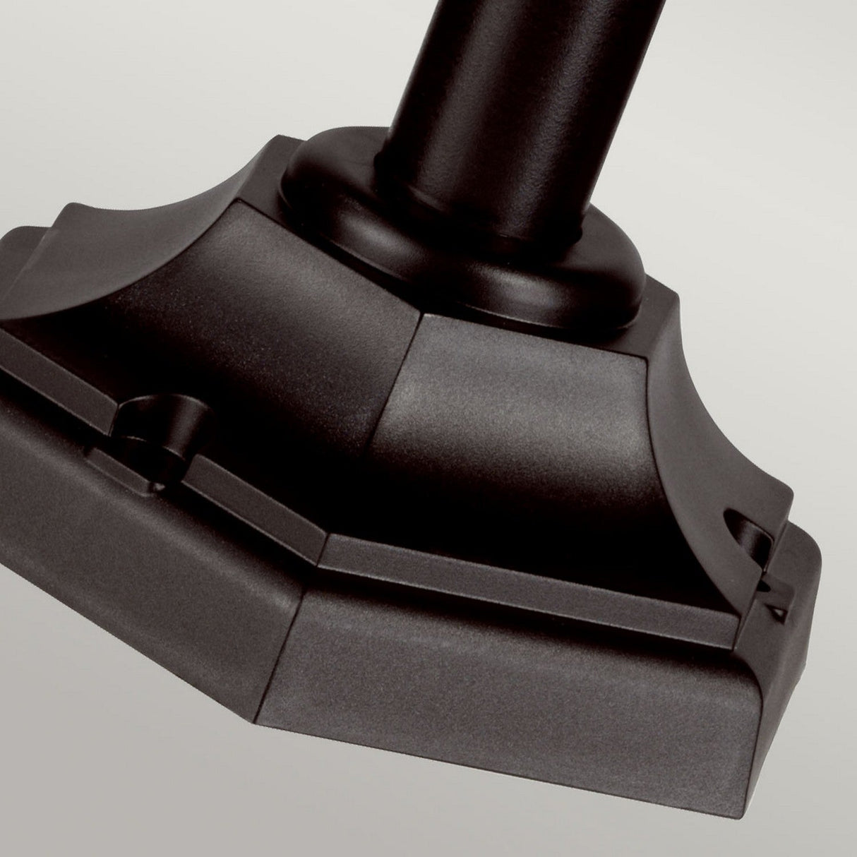 Close-up of the Kerry 1 Light Pillar Light's geometric metal base against a light gray background. This corrosion-proof black base features a rectangular shape with beveled edges and ridged details, making it perfect for outdoor lighting setups.