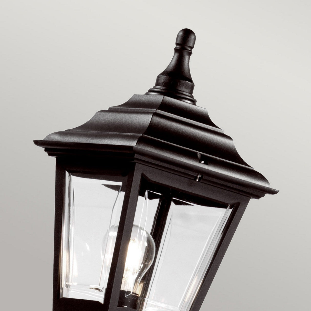The Kerry 1 Light Lamp Post - Black is showcased, ideal for enhancing your outdoor lighting. This lantern boasts a classic design with a tiered, peaked top and clear glass panels that reveal the light bulb inside. With an IP44 rating, it offers reliable durability against various weather conditions. The backdrop features a subtle gray gradient.