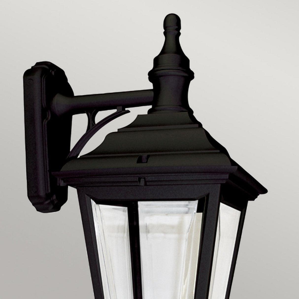 The Kerry 1 Light Outdoor Wall Light in black features a traditional design with a pointed top and clear glass panels, crafted from corrosion-proof black polymer. This IP44-rated fixture is mounted on a rectangular base, making it ideal for exterior lighting.