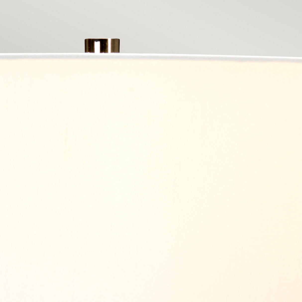 Close-up view of the top portion of a beige lampshade with a metallic finial on a light gray background, beautifully complementing the botanical-inspired base of the Kew 1 Light Table Lamp in Sage Green.