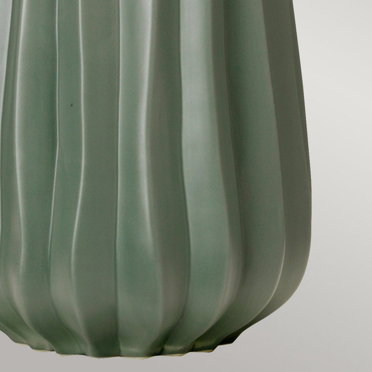 A close-up of the Kew 1 Light Table Lamp in sage green, highlighting its smooth texture and elegant design with vertical grooves. This botanical-inspired piece stands subtly against a soft gray backdrop, enhancing its muted hue.