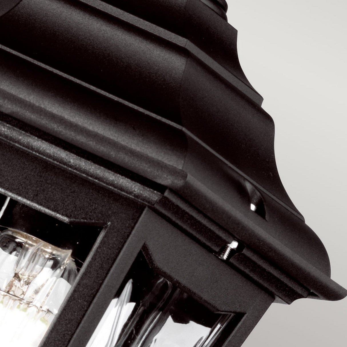 The Kinsale 1 Light Outdoor Chain Pendant in black is captured in a close-up image, highlighting its decorative top. This corrosion-proof pendant light features clear glass panels, revealing the bulb inside against a soft, neutral gray backdrop.