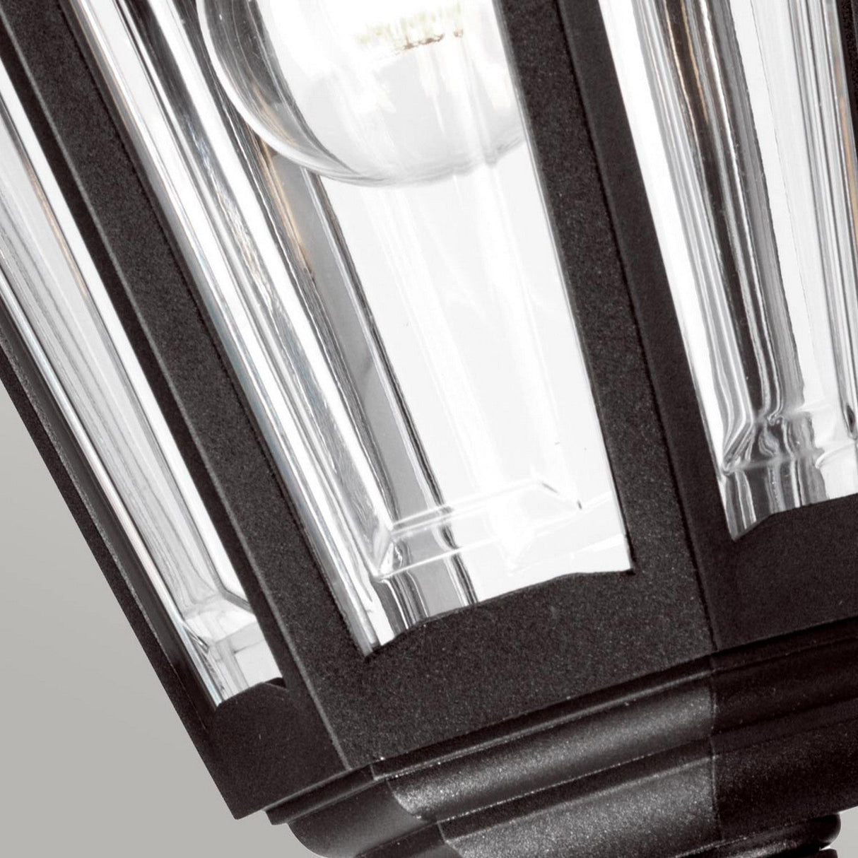 Close-up of the Kinsale 1 Light Outdoor Chain Pendant - Black, which features a visible light bulb encased in its black metal and glass frame. This lantern-style outdoor pendant light has a geometric rectangular design with clear glass panels that highlight the bulb, and its corrosion-proof construction guarantees durability against the elements.
