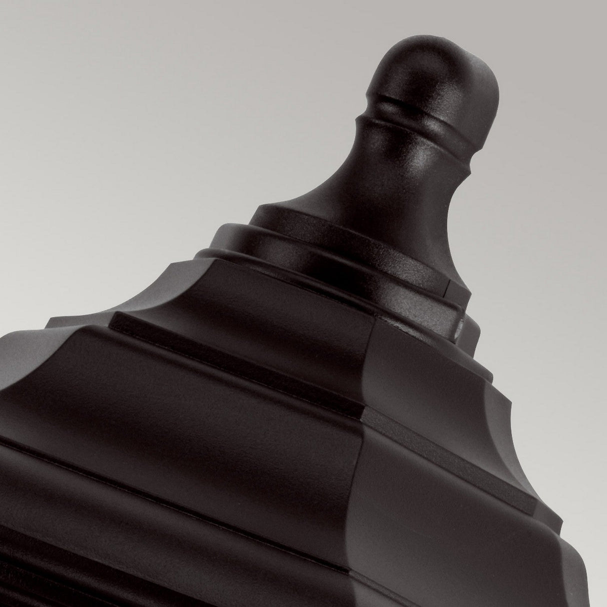 The Kinsale-1 1 Light Outdoor Wall Light in black features a matte-finish metallic design with intricately layered geometric patterns, providing a stylish and durable weather-resistant ornament, perfectly set against a neutral gray background.