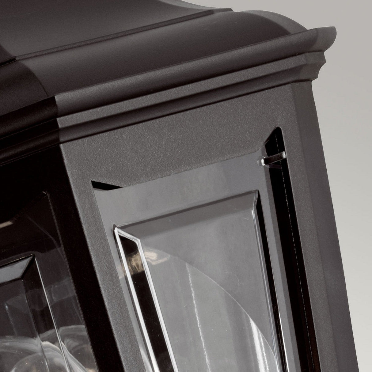 Close-up of the Kinsale-1 1 Light Outdoor Wall Light in black, featuring corrosion-proof design with clear glass panels framed by a sturdy metal structure. The slightly curved top is adorned with decorative edges, highlighting its weather-resistant qualities and intricate details that make this outdoor wall light both functional and stylish.