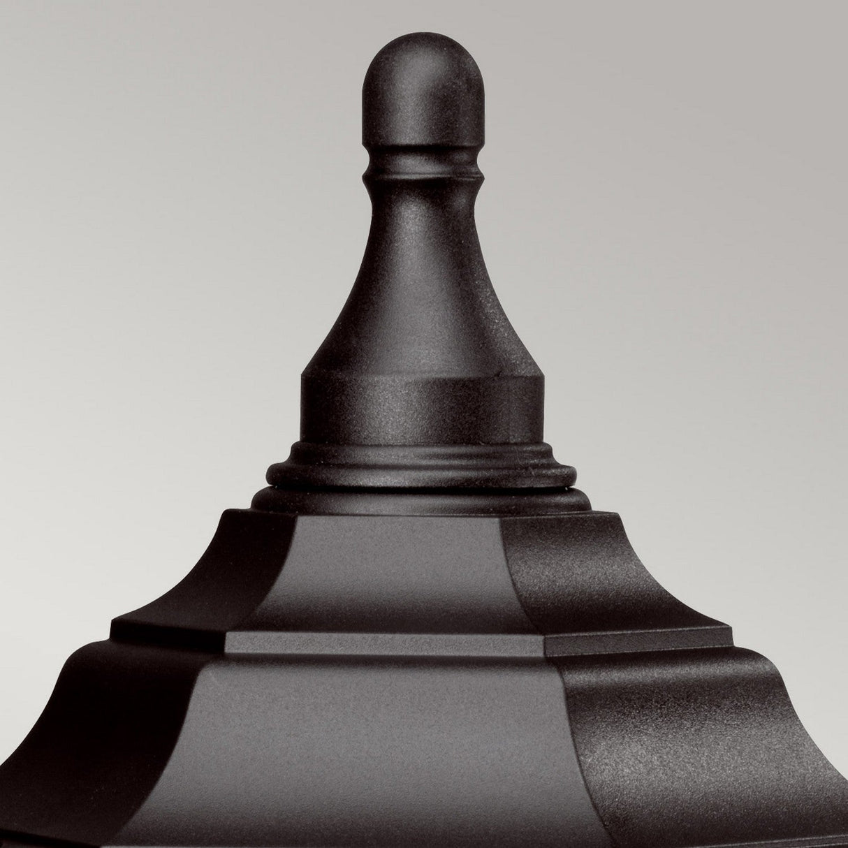 A detailed close-up showcases the Kinsale 1 Light Pedestal/Porch Light in black, featuring an ornate finial with a smooth, rounded top and a layered base designed for corrosion resistance. Ideal for outdoor lighting, it contrasts beautifully against a plain gray background.