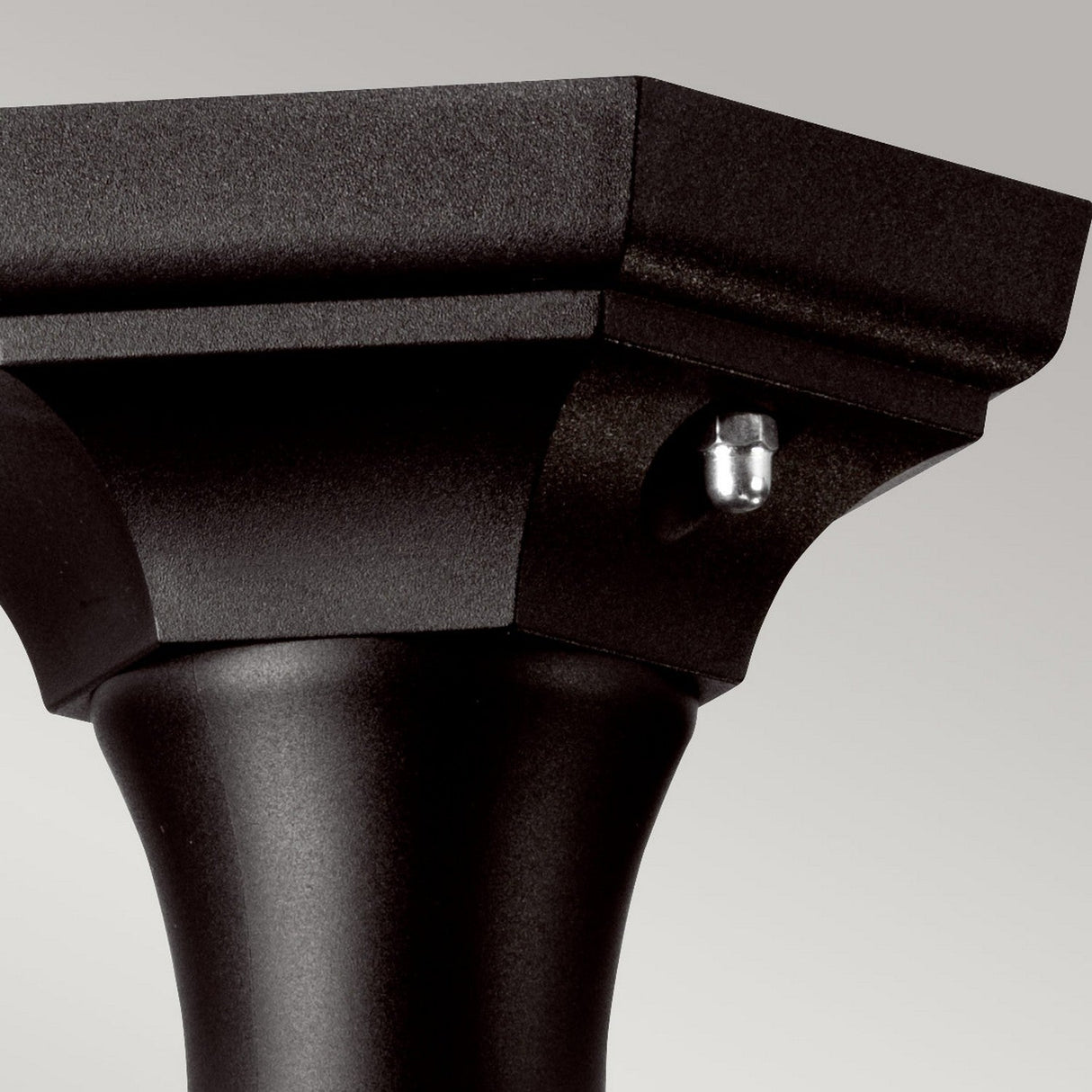 Close-up of the Kinsale 1 Light Pedestal/Porch Light in black, showcasing its black metal finial with a square, tiered top. The corrosion-proof finial features a decorative bolt on one side and a smooth, slightly curved stem, making it ideal for outdoor lighting. It is set against a plain, light gray background.