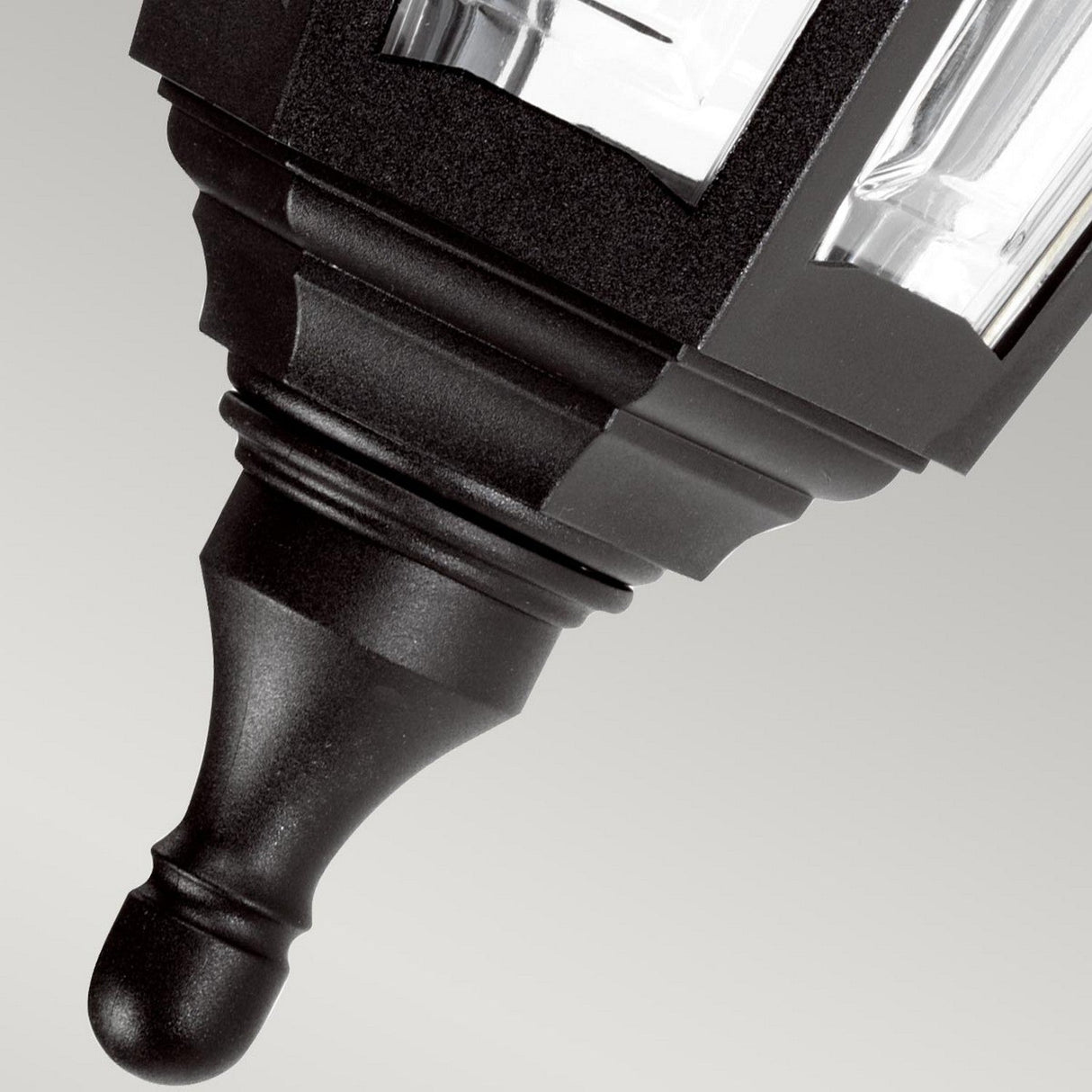 Close-up of the corrosion-proof, ornate top of the Kinsale-2 1 Light Outdoor Wall Light in black, featuring decorative elements and clear panels, designed to withstand coastal environments, set against a neutral background.