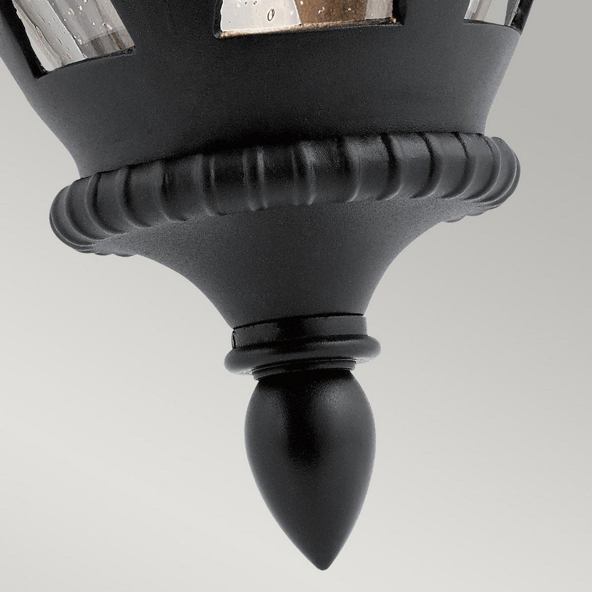 Close-up of the Admirals Cove Outdoor 1 Light Large Wall Lantern, featuring a Tudor-inspired design with a black, ribbed finish and a finial at the bottom. The top section highlights reflective glass panels, set against a smooth gray background.