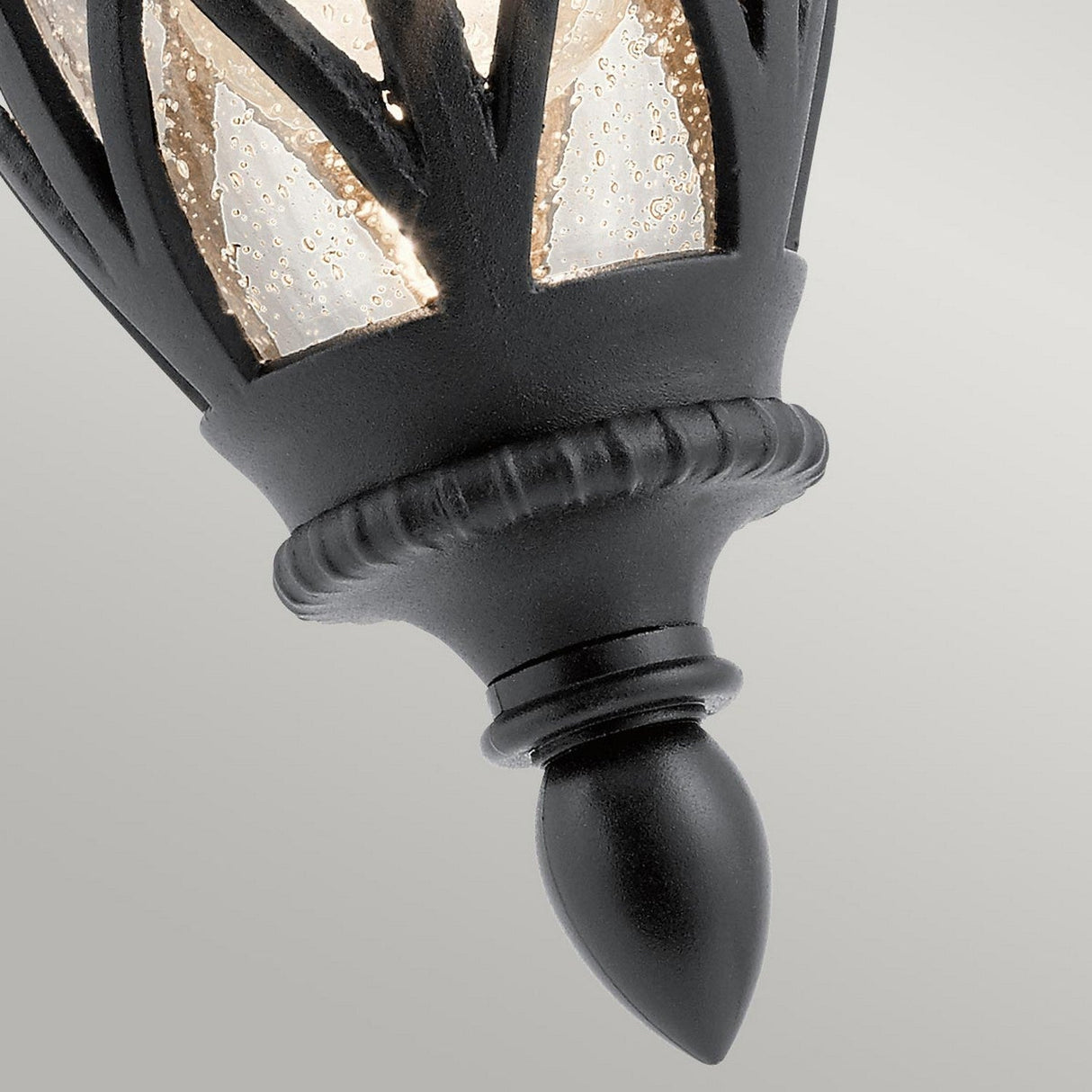 A close-up of the Admirals Cove Outdoor 1 Light Small Wall Lantern in black reveals its textured metal frame and frosted glass panels. The bubble-like texture of this IP44 rated lamp enhances its charm as it points downward, highlighting its intricate design against a light gray background.