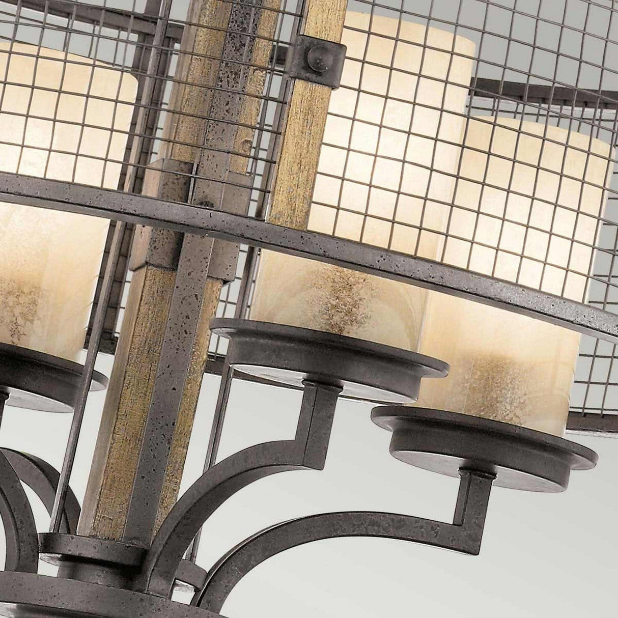 A close-up of the Ahrendale 4 Light Chandelier - Grey, featuring cylindrical frosted glass shades. This fixture showcases a grid-like Anvil Iron mesh frame, offering rustic charm and a modern, elegant aesthetic.