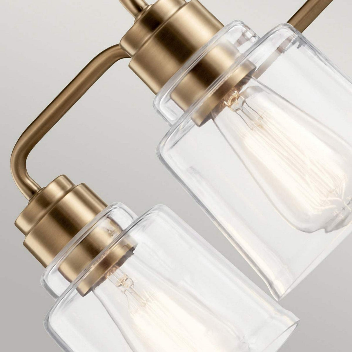 The Aivian 5 Light Chandelier in weathered brass features clear glass shades that showcase exposed filament bulbs, casting a warm glow against a neutral background and adding an industrial style charm.