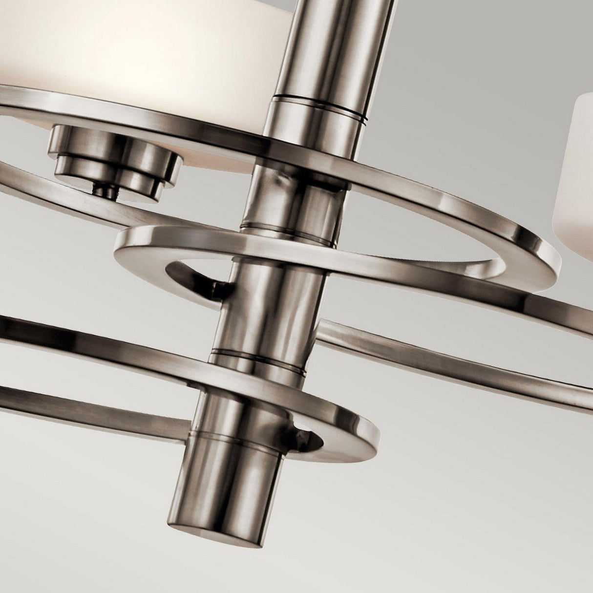The Aleeka 3 Light Chandelier in silver showcases a sleek, brushed nickel finish with circular bands and cylindrical light fixtures. Its design exemplifies contemporary lighting against a neutral background, making it perfect for modern interiors.