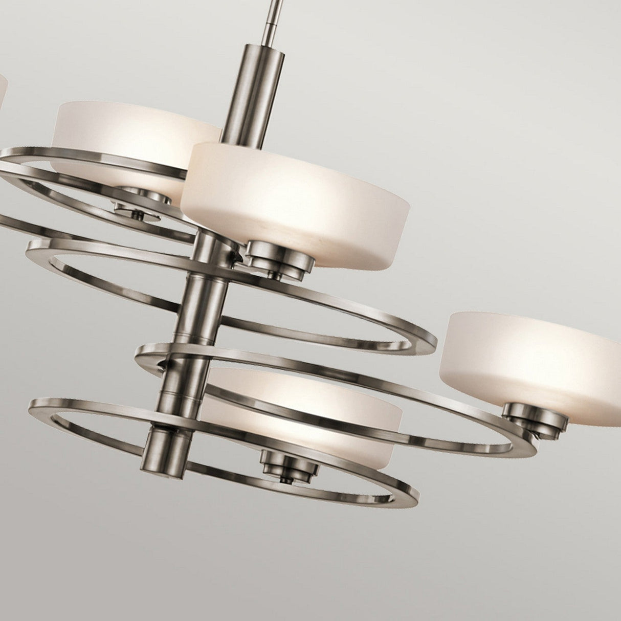 The Aleeka 5 Light Chandelier - Silver, with its celestial inspiration, showcases circular brushed metal frames and frosted glass shades. Its sleek, symmetrical design perfectly complements contemporary interiors against a light grey background.