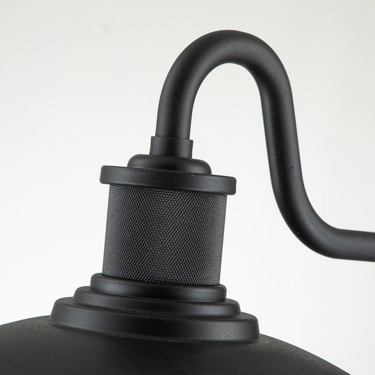 Close-up of the Allenbury Outdoor 1 Light Medium Wall Lantern - Black, showcasing an IP44 rated black metal fixture with a round base and curved arm. This outdoor wall lantern features a textured, cylindrical central piece that provides weather-resistant lighting against a plain, light background.