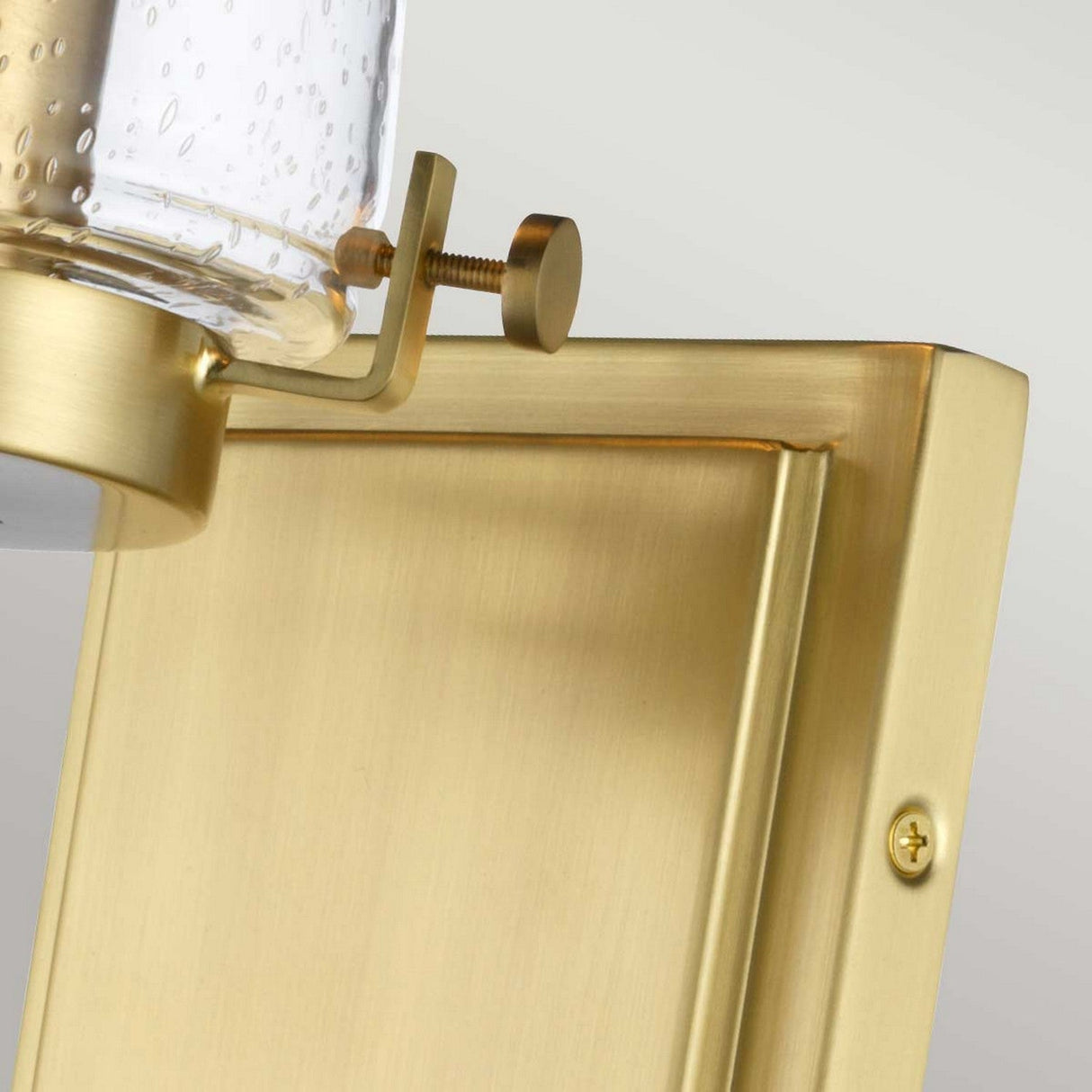 Detailed view of the Alton 1 Light Wall Light in brushed brass, showcasing its gold-colored sconce design with a textured glass shade, ideal for elevating bathroom decor. This fixture exudes industrial-era charm, mounted on a rectangular brushed brass backplate and adorned with a decorative brass screw on top.