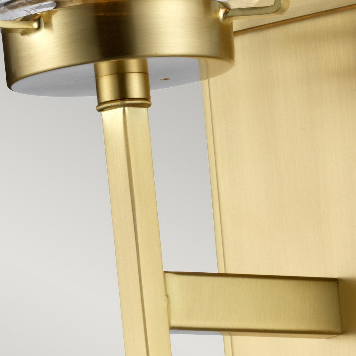 A close-up of the Alton 1 Light Wall Light in brushed brass showcases its angular design and matte finish. The fixture's geometric shape exudes industrial-era charm, especially when highlighted against a light gray background, making it an ideal choice for sophisticated bathroom decor.