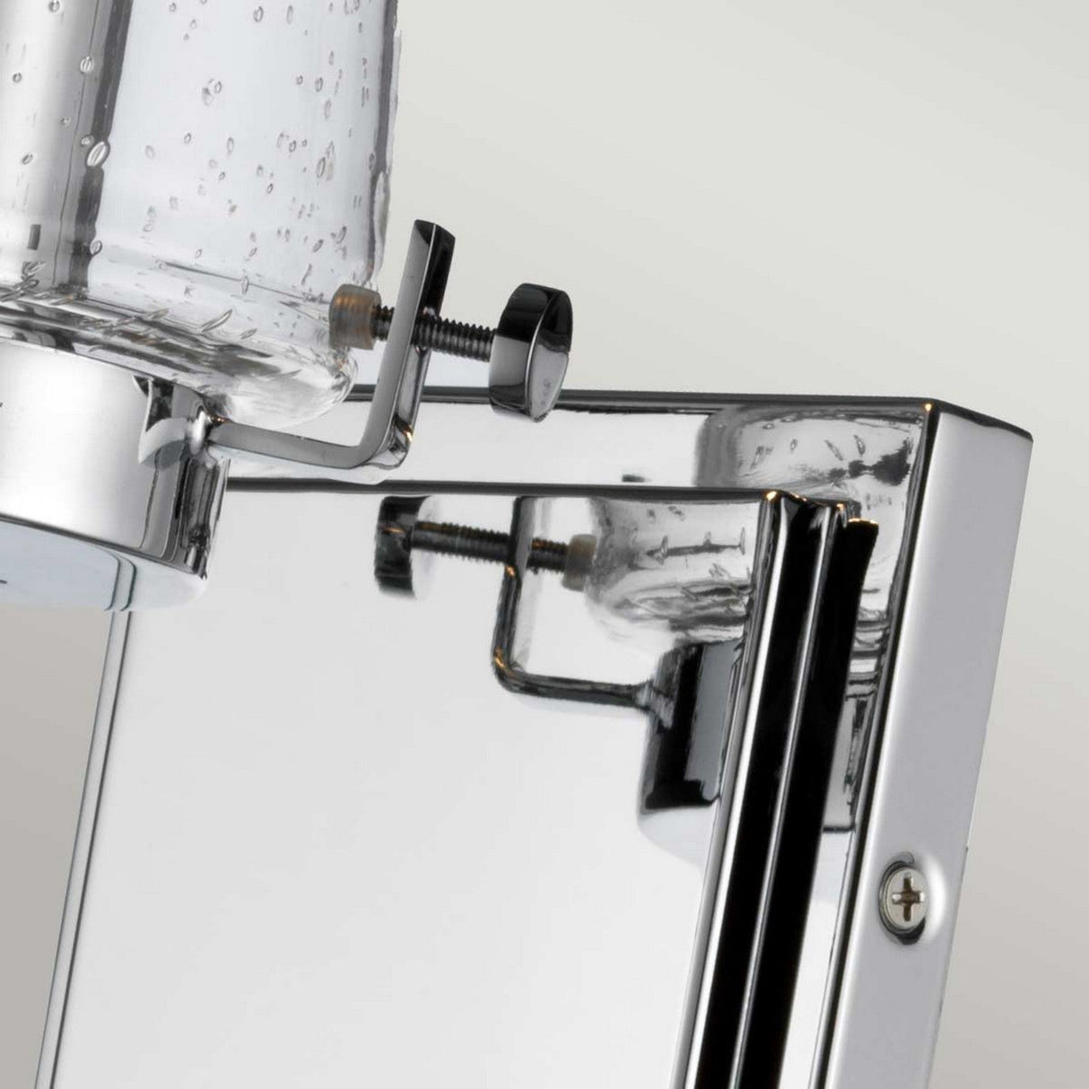 Detailed view of the Alton 1 Light Wall Light in chrome paired with textured glass, installed on a glossy metallic panel. This IP44 rated fixture highlights contemporary design features with visible screws and connectors, ideal for industrial-style bathroom lighting.