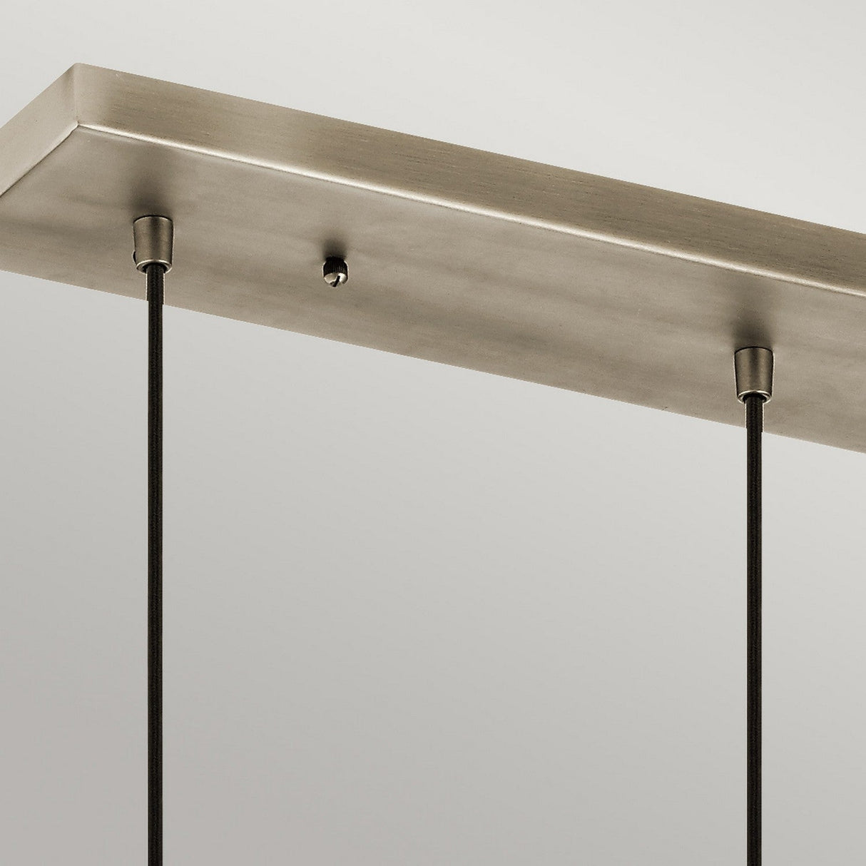 Close-up of the Asher 3 Light Pendant Rectangle - Silver, featuring a rectangular metallic ceiling mount with two black cords hanging down. The fixture's brushed finish and small central screw enhance its modern industrial aesthetic against a plain light gray backdrop.