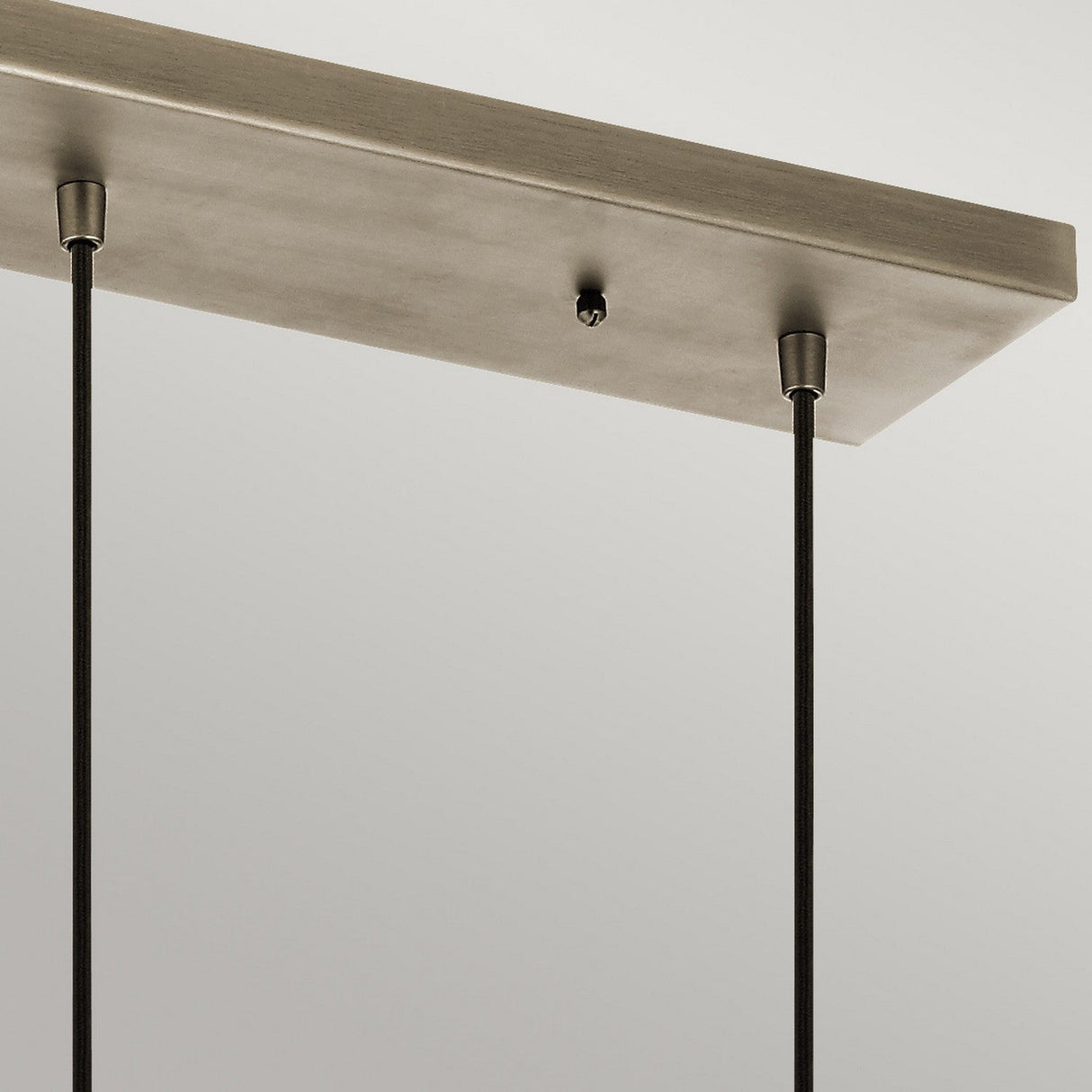 A close-up view of the Asher 3 Light Pendant Rectangle - Silver showcases a metallic ceiling fixture with two black cords hanging against a neutral background. The cords connect to a rectangular metal plate, embodying an industrial lighting style for a distinctly modern look.