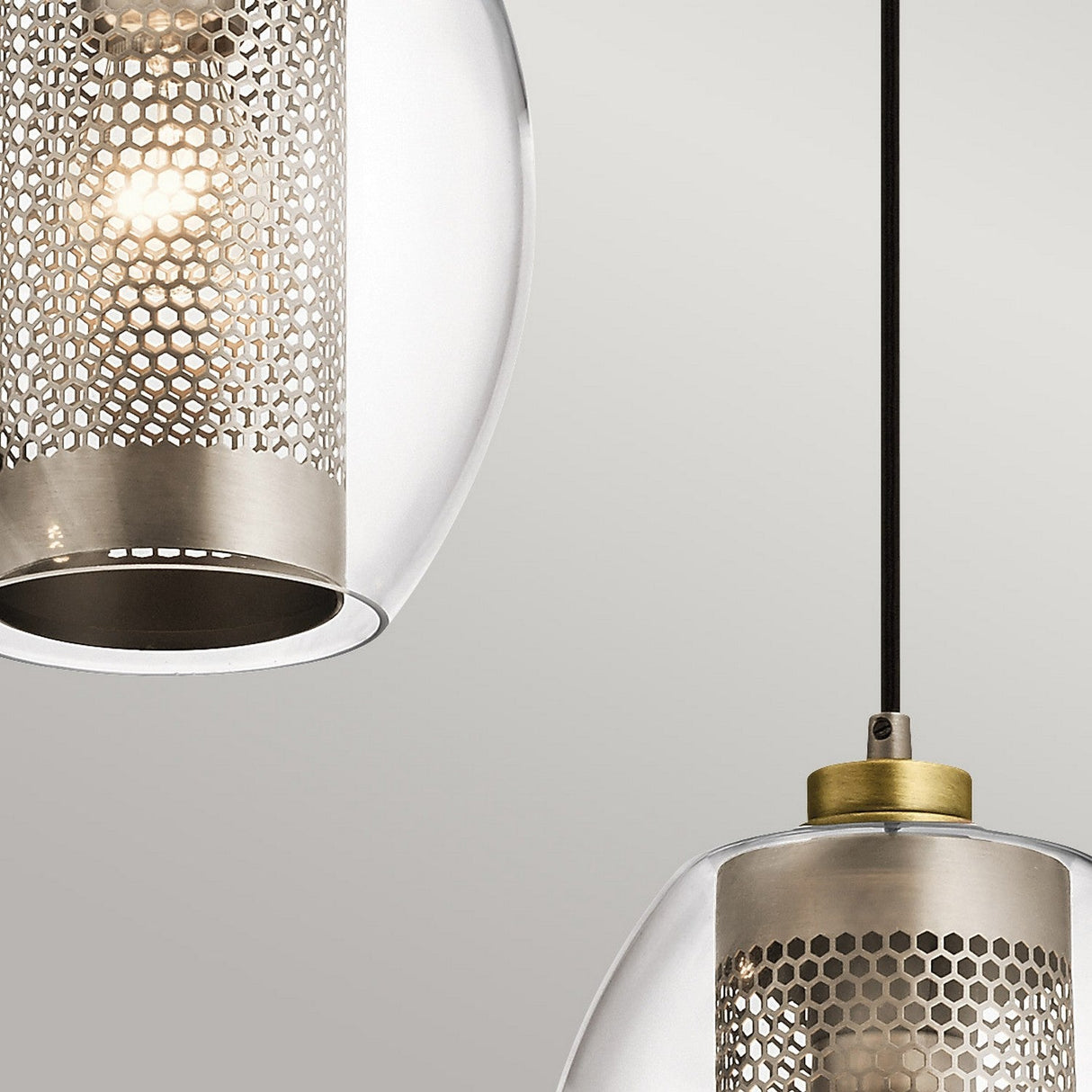 The Asher 3 Light Pendant Rectangle - Silver creates a sleek, modern ambiance with its three contemporary pendant lights. It features cylindrical mesh metal shades encased in clear glass exteriors, each suspended from a black cord. These lights cast a warm, soft glow against the plain, light gray surface for an industrial lighting vibe.