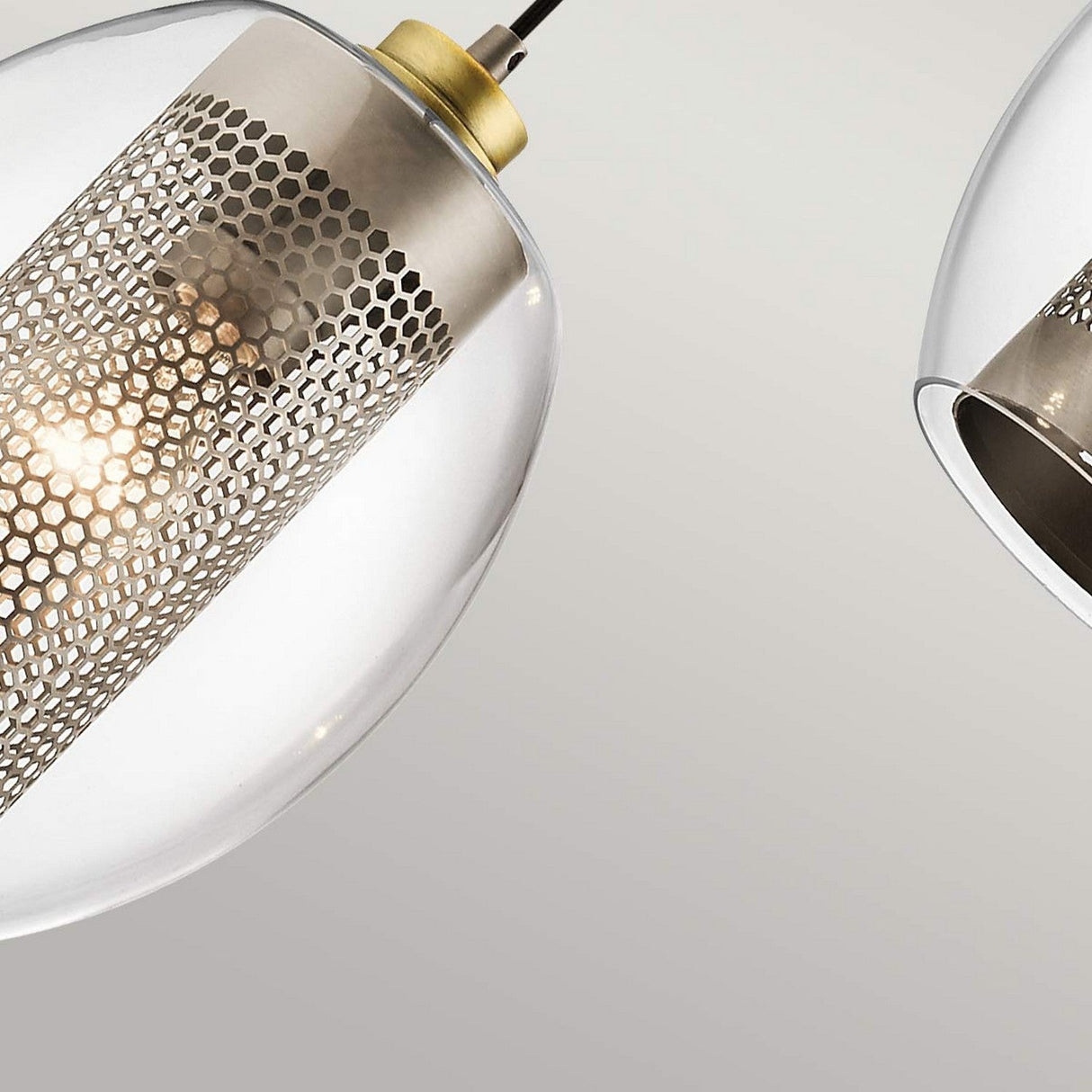 Close-up of two Asher 1 Light Mini Pendants - Silver, showcasing their modern design with transparent glass shades and metallic mesh inserts. The pendant on the left is illuminated, emitting a warm glow that captures the essence of industrial-inspired lighting against a soft gradient of light gray in the background.