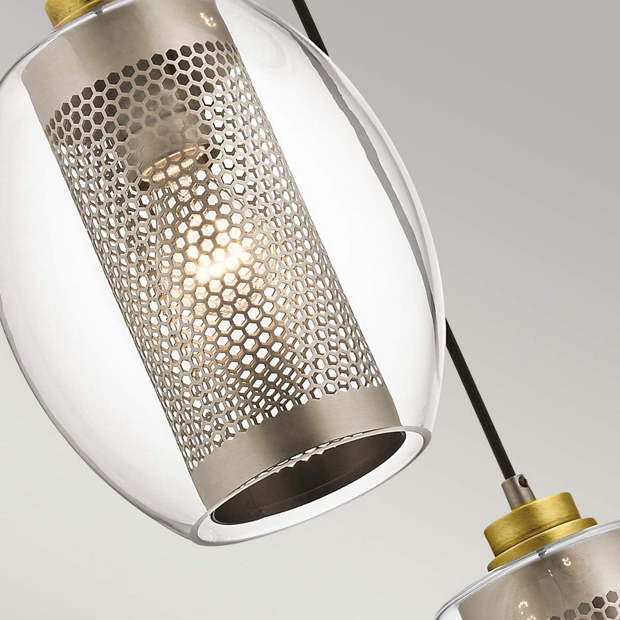Close-up of two Asher 1 Light Mini Pendants - Silver, featuring transparent glass shades and perforated metal interiors. This industrial-inspired lighting with a modern design casts intricate patterns against a soft gradient background.
