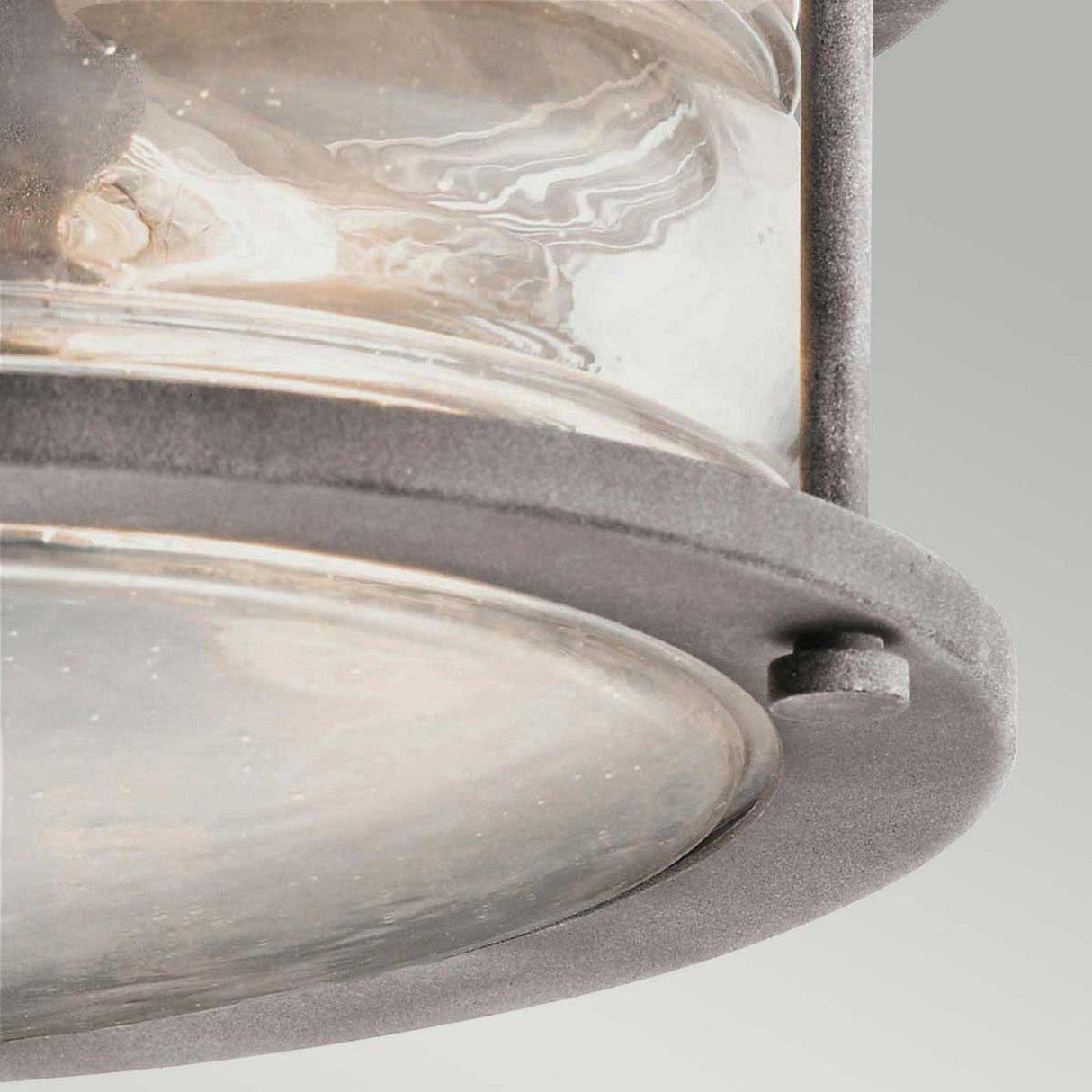 Close-up view of the Ashland Bay Outdoor 2 Light Outdoor Ceiling Flush, featuring a circular design. The image highlights the detailed textures of the clear seeded glass and metal components, showcasing the craftsmanship in this weathered zinc fixture.