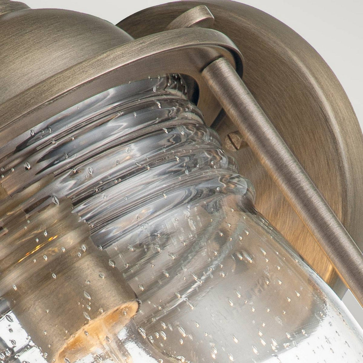 Close-up of the Ashland Bay Outdoor 1 Light Large Wall Lantern - Burnished Bronze. This vintage-style wall light showcases a burnished bronze finish with a clear, textured glass shade that contains visible air bubbles, encasing an LED Edison-style bulb for a classic, rustic appearance.