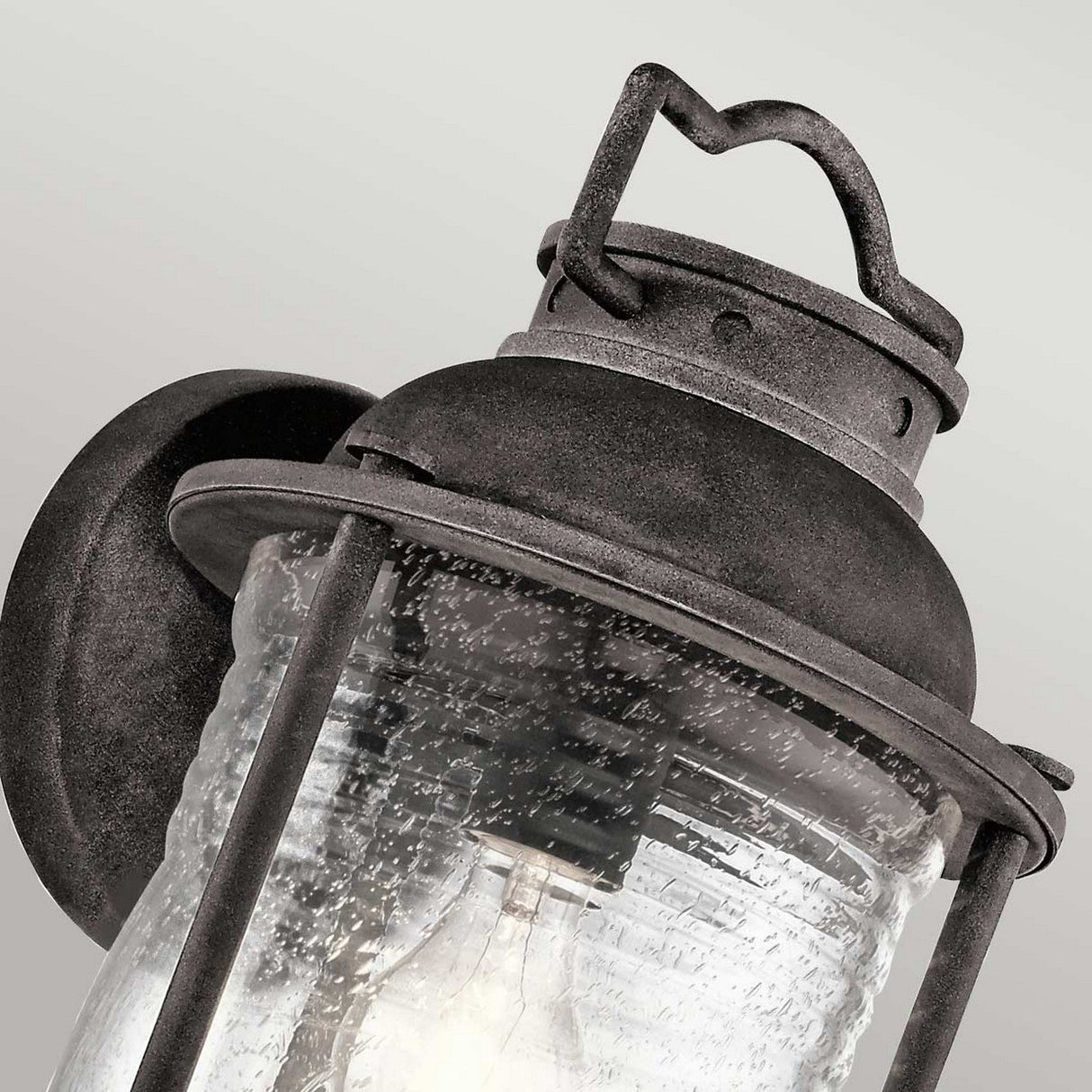A detailed view of the Ashland Bay Outdoor 1 Light Large Wall Lantern, showcasing its weathered zinc frame and glass panels. The lantern includes a textured finish and houses an LED Edison bulb, set against a simple light gray background.