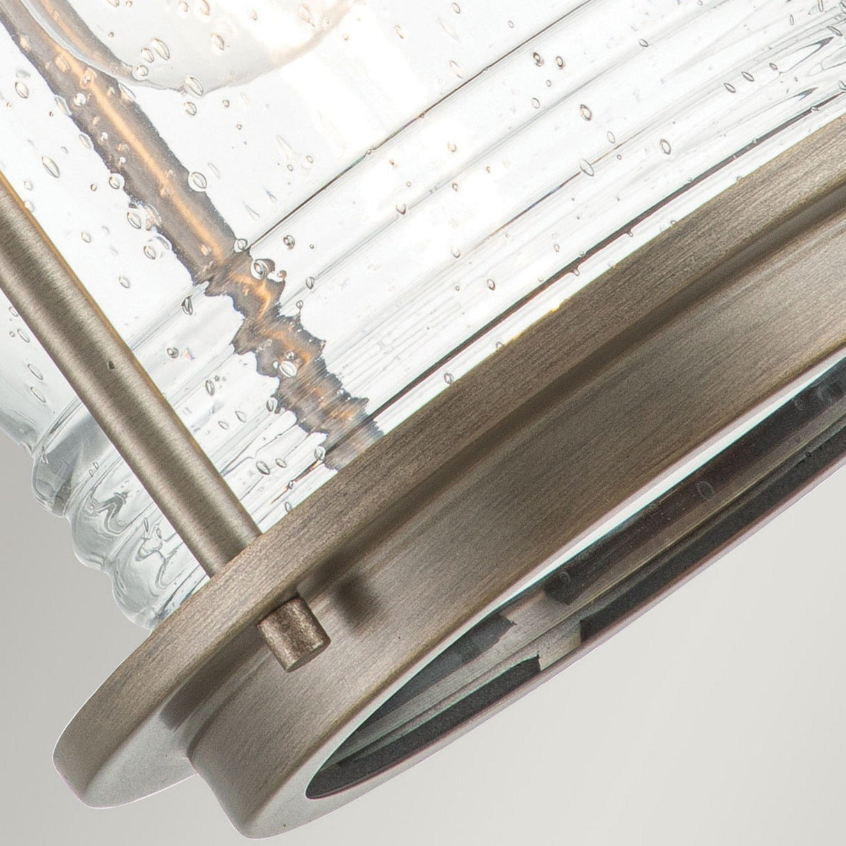 The Ashland Bay Outdoor 1 Light Medium Wall Lantern in Burnished Bronze features a close-up view of bubbles in its clear seeded glass. This fixture's metal frame, complete with a cylindrical rod design and circular base, showcases its distinct textures and materials, making it ideal for an elegant outdoor wall lantern setting.