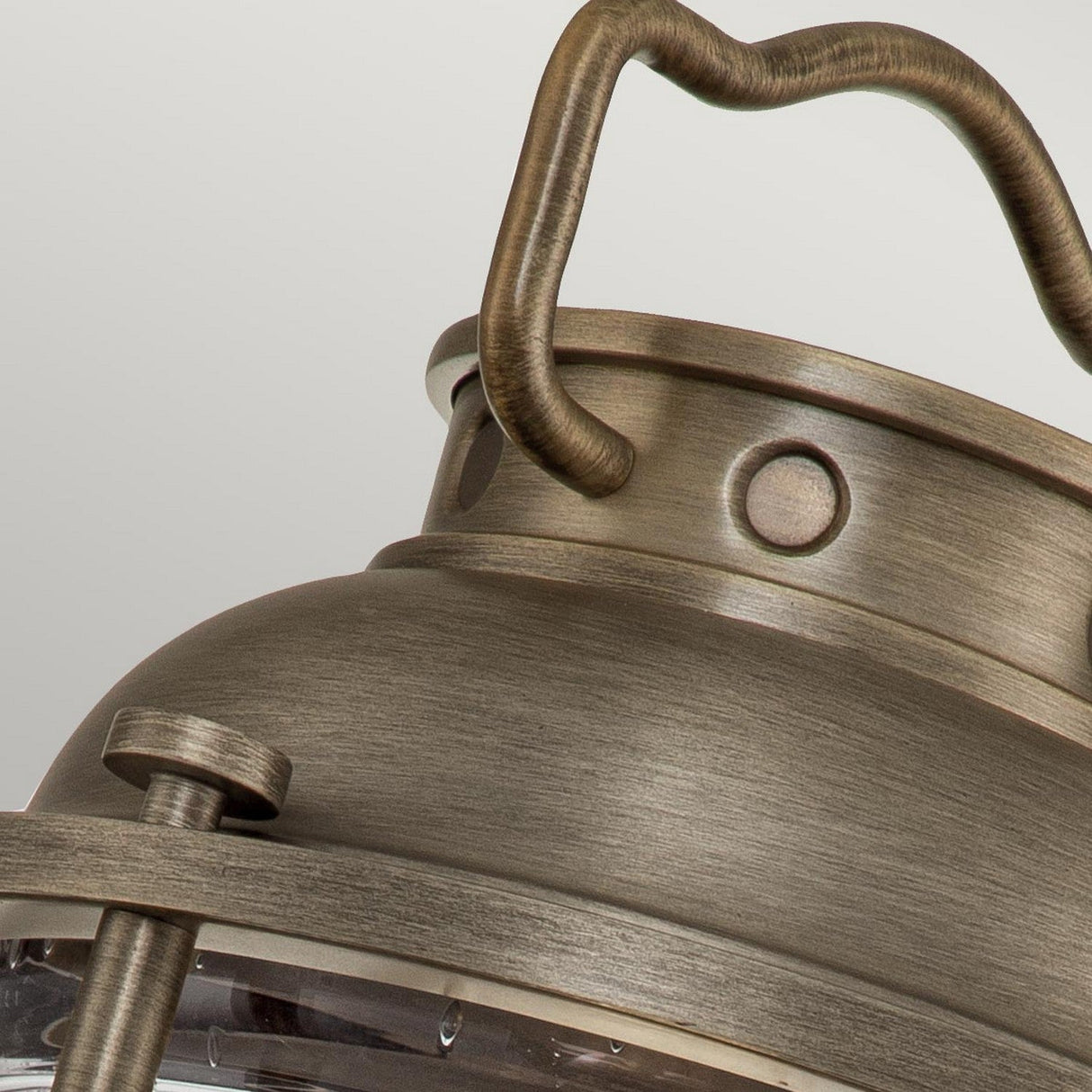 A close-up view showcases the Ashland Bay Outdoor 1 Light Medium Pedestal Lantern in burnished bronze, highlighting its vintage-style metallic design with a curved handle, rivet-like details, and a brushed finish. Inside, an LED Edison bulb emits a warm glow against a neutral backdrop.