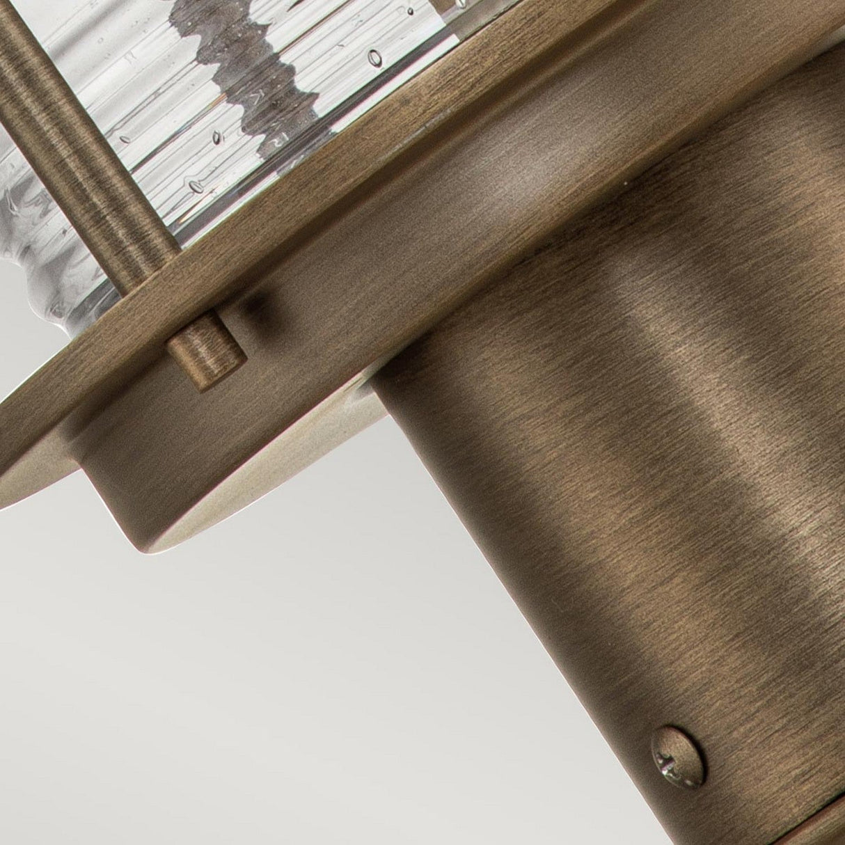 Close-up of the Ashland Bay Outdoor 1 Light Medium Pedestal Lantern in Burnished Bronze, showcasing a cylindrical glass cover and textured surface. Its intricate details are highlighted by a burnished bronze finish, with a modern design complemented by the warm glow of an LED Edison bulb that emphasizes its sleek, industrial aesthetic.