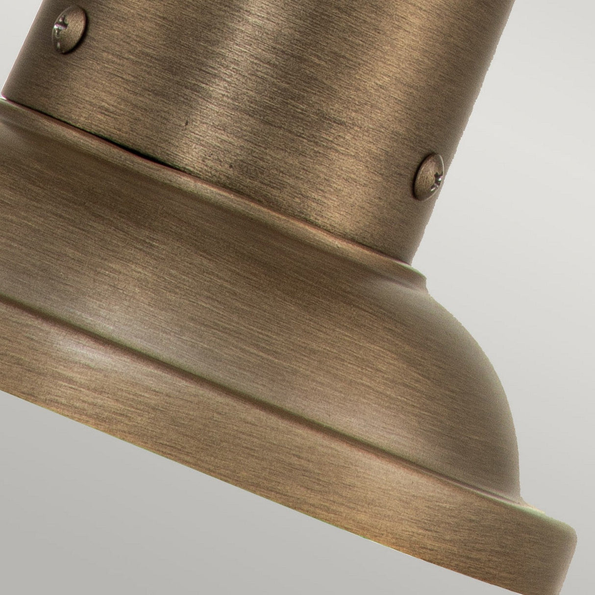 Close-up of the Ashland Bay Outdoor 1 Light Medium Pedestal Lantern in burnished bronze, showcasing its metallic surface with two screws and a cylindrical shape. The texture conveys a sturdy, industrial design typical of an outdoor pedestal lantern against a subtle, neutral background.