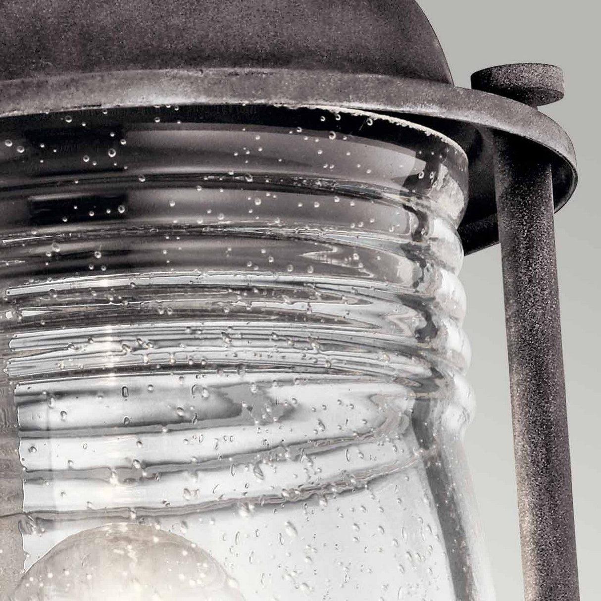 The Ashland Bay Outdoor 1 Light Medium Pedestal Lantern in Weathered Zinc boasts vintage charm with its weathered zinc metal frame and clear glass casing. The textured droplets on the glass enhance its aged appearance, while an LED Edison-style bulb inside adds nostalgic warmth to the rustic design.