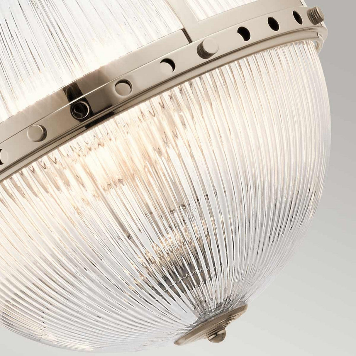 Close-up of the Aster 3 Light Pendant - Polished Nickel, showcasing its modern design with ribbed glass domes. The fixture boasts a metallic band with circular cutout details, enhancing the light's warm glow against a neutral background.