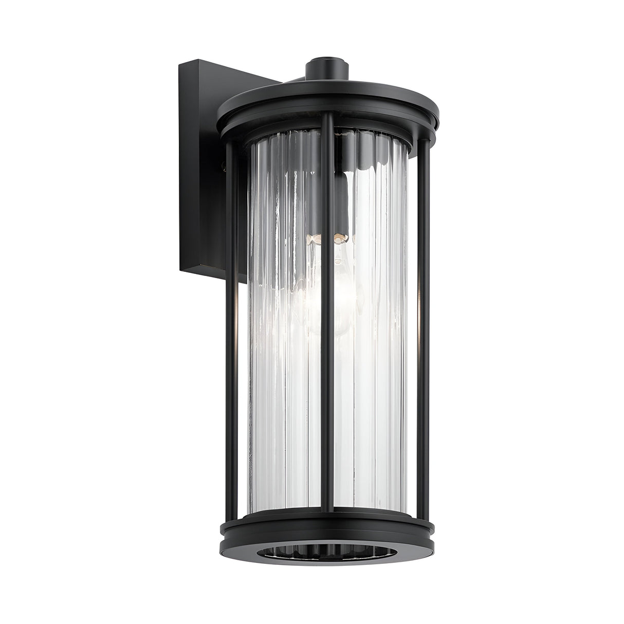Introducing the Barras Outdoor 1 Light Medium Wall Lantern in Black. This contemporary wall lantern flaunts a sleek cylindrical design with ribbed glass casing that elegantly reveals a single light bulb inside. Mounted on a rectangular base, it effortlessly blends style and functionality for your outdoor lighting needs.