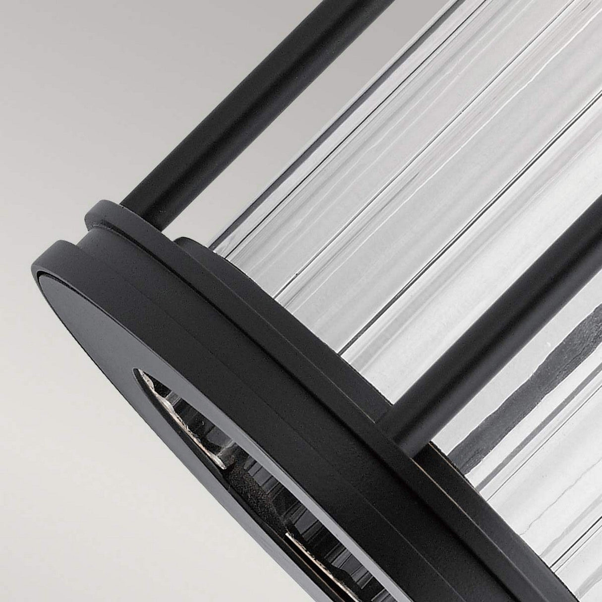 Close-up of the Barras Outdoor 1 Light Small Wall Lantern in Black, featuring a cylindrical shape with vertical grooves and black metal accents, set against a light gray background. The fixture combines modern design with vintage charm.