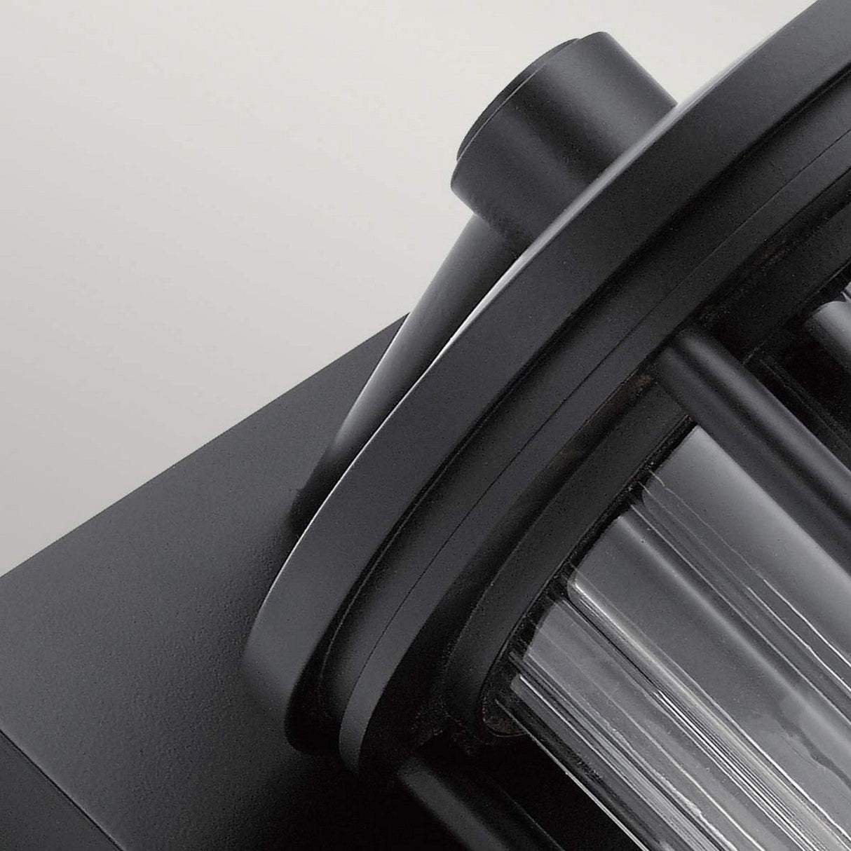 Close-up of the Barras Outdoor 1 Light Small Wall Lantern in black, reminiscent of vintage charm. It features a sleek design with a clear glass enclosure, harmonizing contemporary and functional aesthetics against a light gray background.