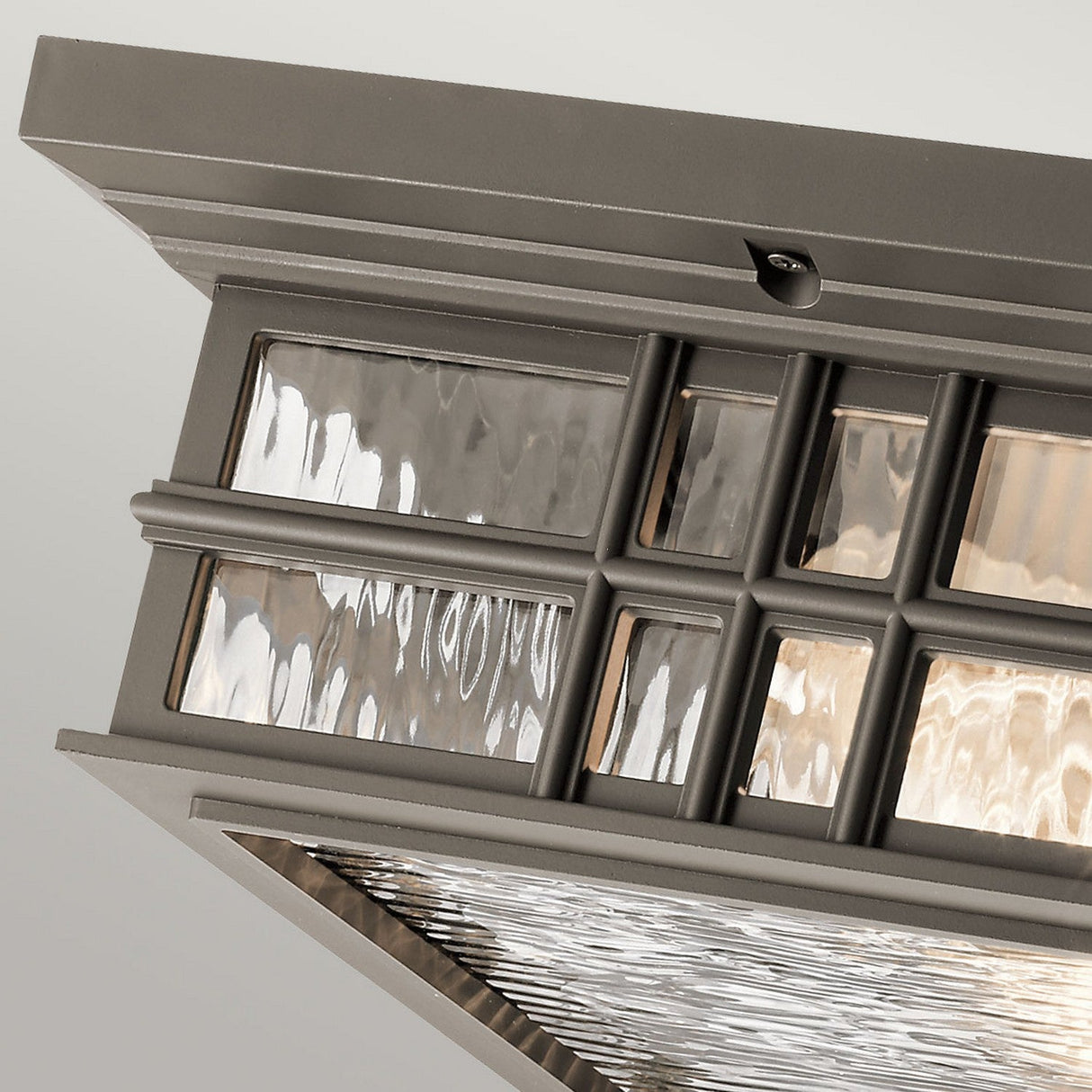 Close-up of the Beacon Outdoor 2 Light Flush with a metal frame featuring an Olde Bronze finish and a grid pattern. Echoing craftsmen architecture, the fixture boasts clear textured glass that allows light to shine through, creating beautiful reflections. It is designed for ceiling mounting.