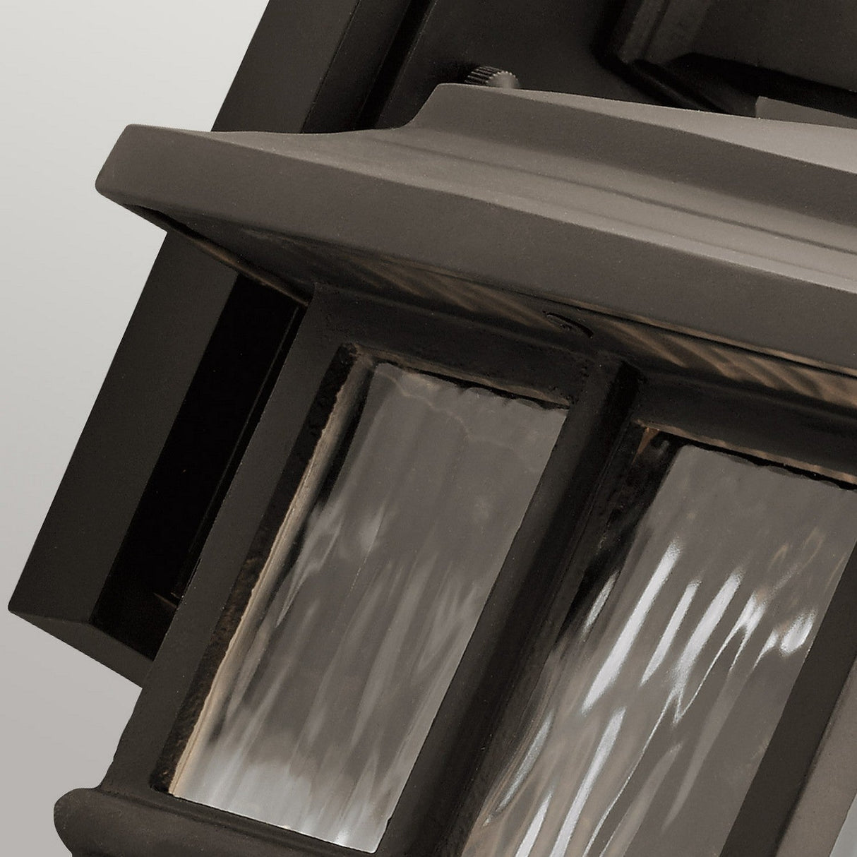 Zoomed-in shot of the Beacon Square Outdoor 1 Light Medium Wall Lantern, showcasing its IP44 durability rating. The lantern features clear, textured glass panels and a metal frame with a modern and sleek dark bronze finish. The rippled texture of the glass enhances its distinctive look.