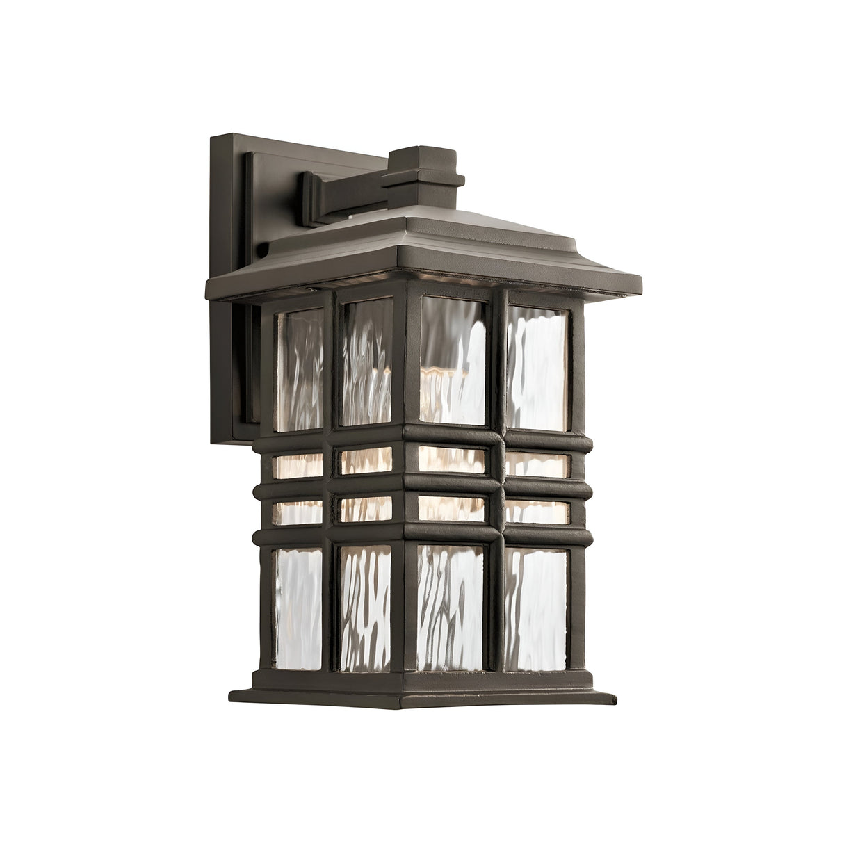 The Beacon Square Outdoor 1 Light Small Wall Lantern - Bronze is a craftsman-inspired fixture featuring a metal frame and clear glass panels. Its bronze design showcases geometric lines and traditional style, housing a light bulb that casts a warm glow.