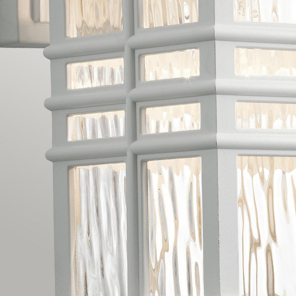 A detailed view of the Beacon Square Outdoor 1 Light Small Wall Lantern in white, highlighting its textured glass panels with a craftsman-inspired design. The glass features a ripple effect that reflects light beautifully, creating a warm and inviting atmosphere while being UV resistant.