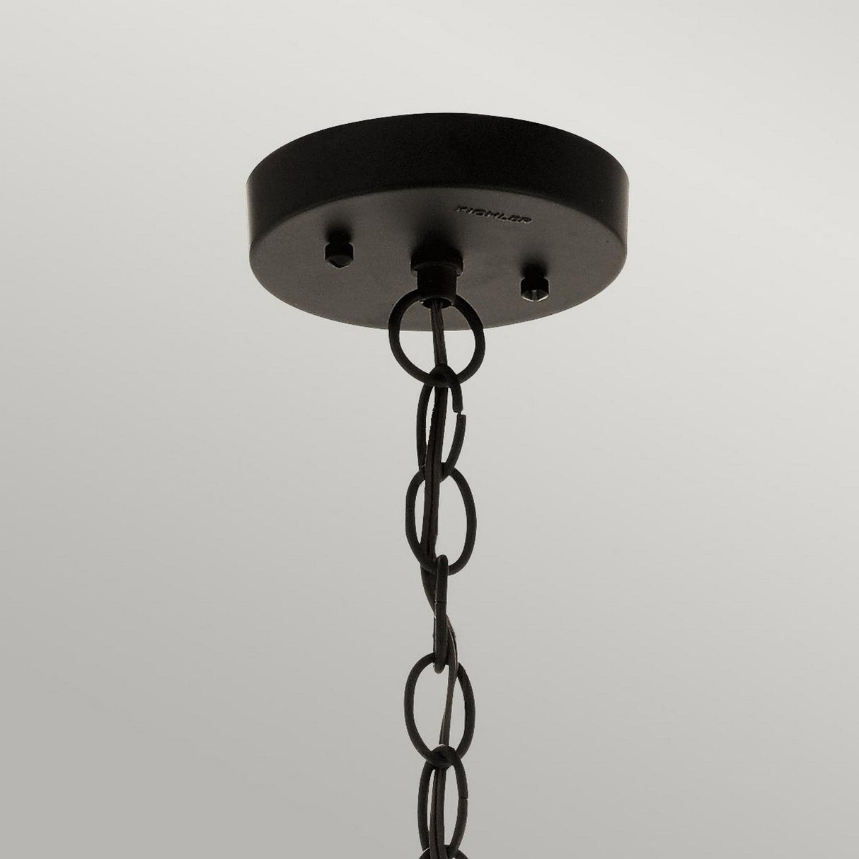 A close-up of a bronze ceiling light fixture base, reminiscent of the Beacon Square Outdoor 1 Light Chain Lantern, features a chain with circular links hanging down. The background is a uniform light gray, enhancing the fixture's elegance.