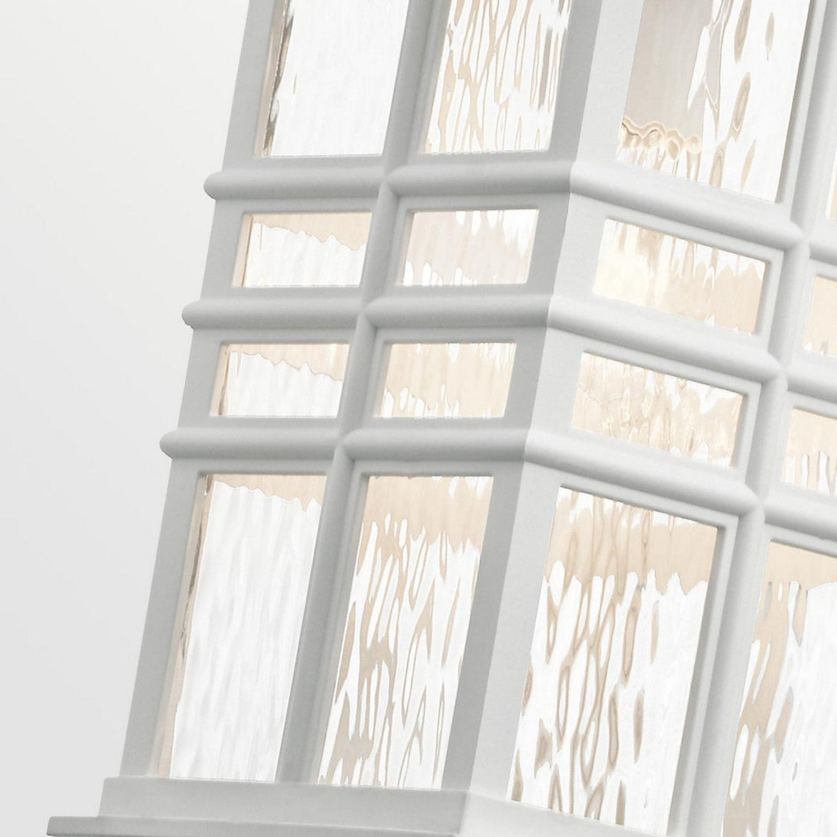 Close-up of a window with frosted, textured glass panes framed in white. The wavy pattern distorts light, creating a craftsman-inspired style that harmonizes modern and classic elements. The scene evokes the gentle glow reminiscent of the Beacon Square Outdoor 1 Light Chain Lantern - White through clear hammered glass.