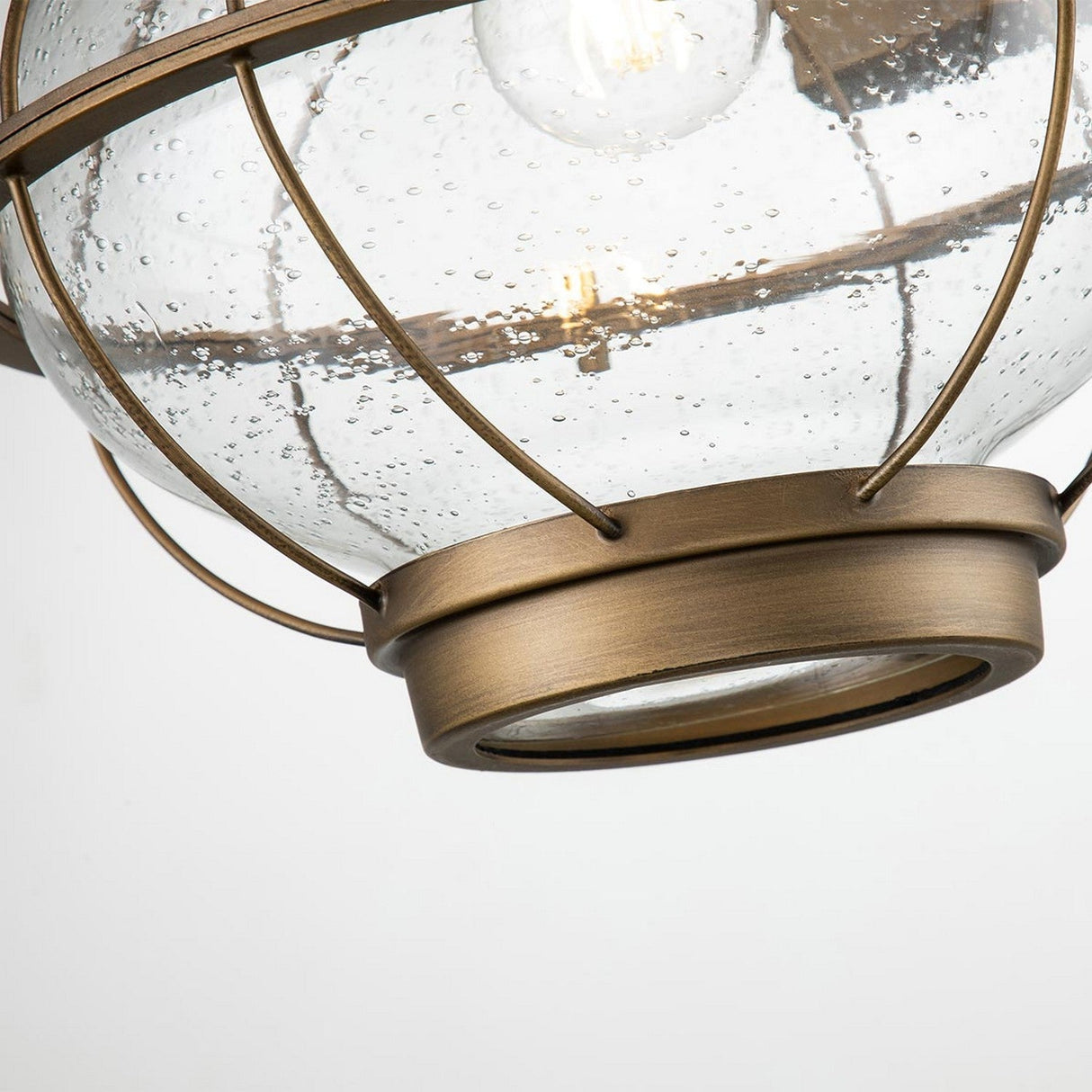 A detailed view of the Bridgepoint Outdoor 1 Light Large Wall Lantern showcasing its spherical, clear glass shade with small bubbles and a visible bulb inside. The lantern features a natural brass-colored metal frame adorned with circular accents, bringing a sense of nautical lighting charm.