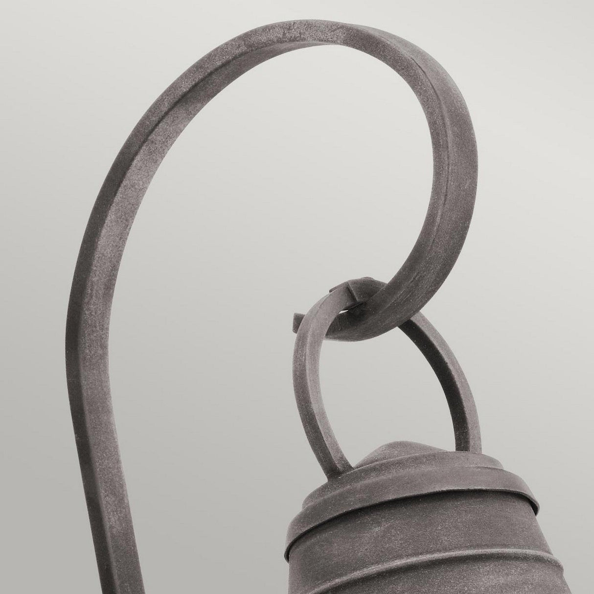 A close-up of the Bridgepoint Outdoor 1 Light Large Wall Lantern in weathered zinc, elegantly suspended from a curved iron hanger against a light, neutral background. This outdoor lighting piece boasts an antique-looking finish that enhances its timeless charm.